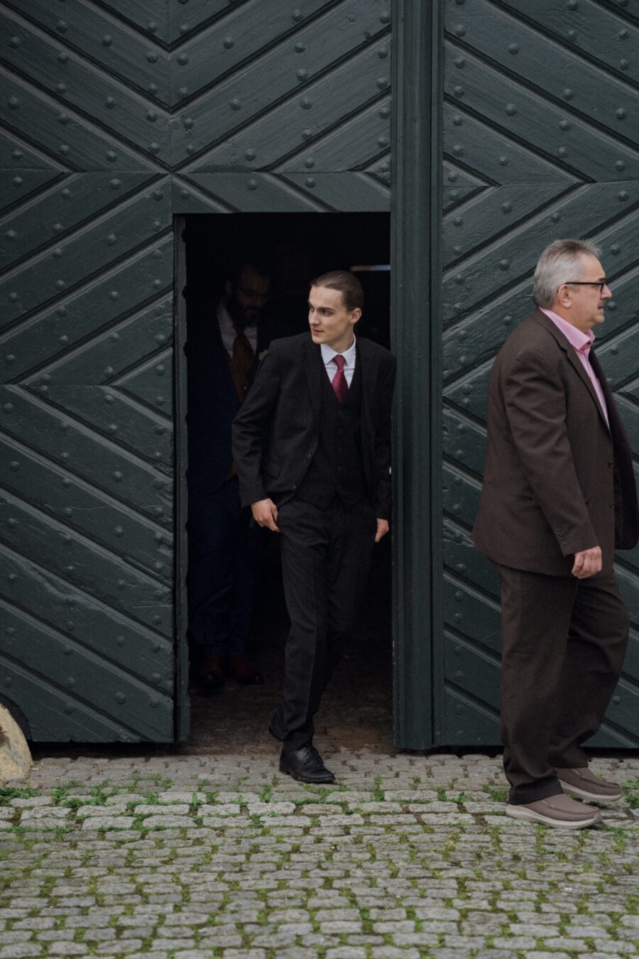 Gäste in Anzügen vor rustikalem Tor