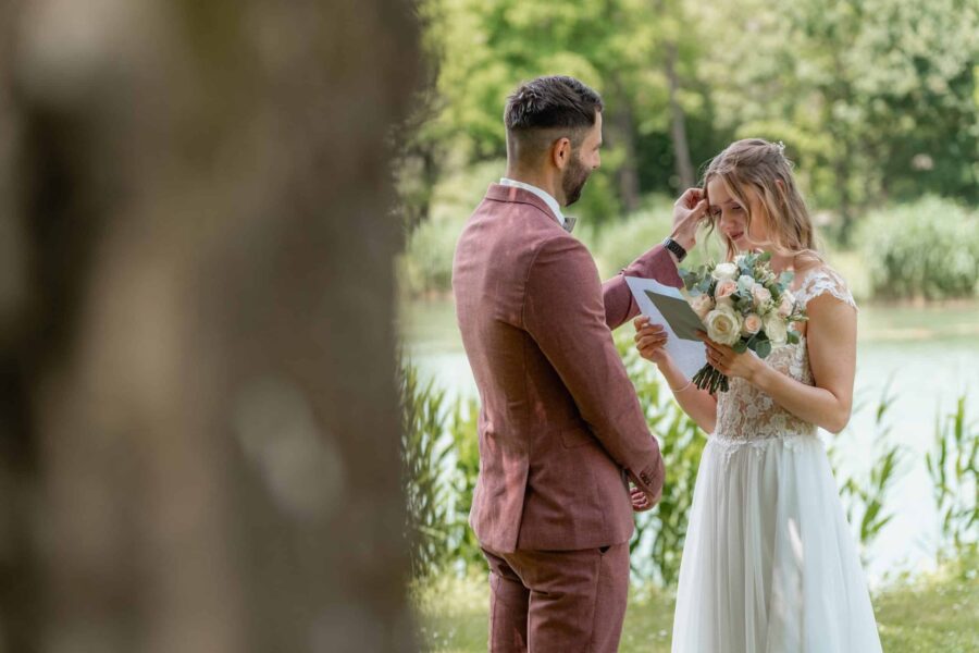 Brautpaar liest Gelübde am Seeufer im Freien.