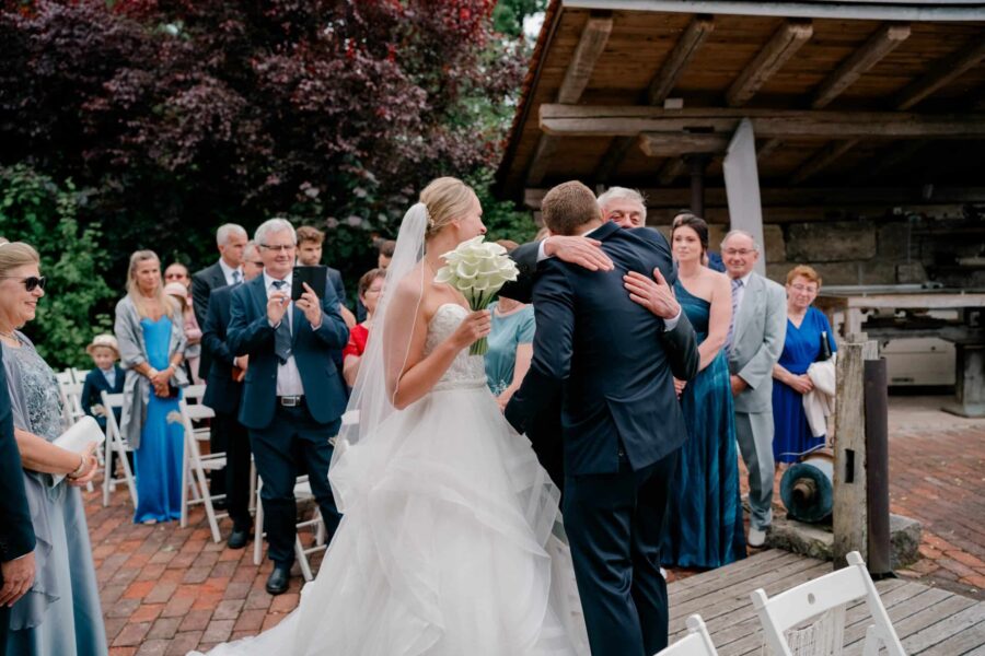 Außenhochzeit mit Bräutigam und Gästen in festlicher Umgebung.