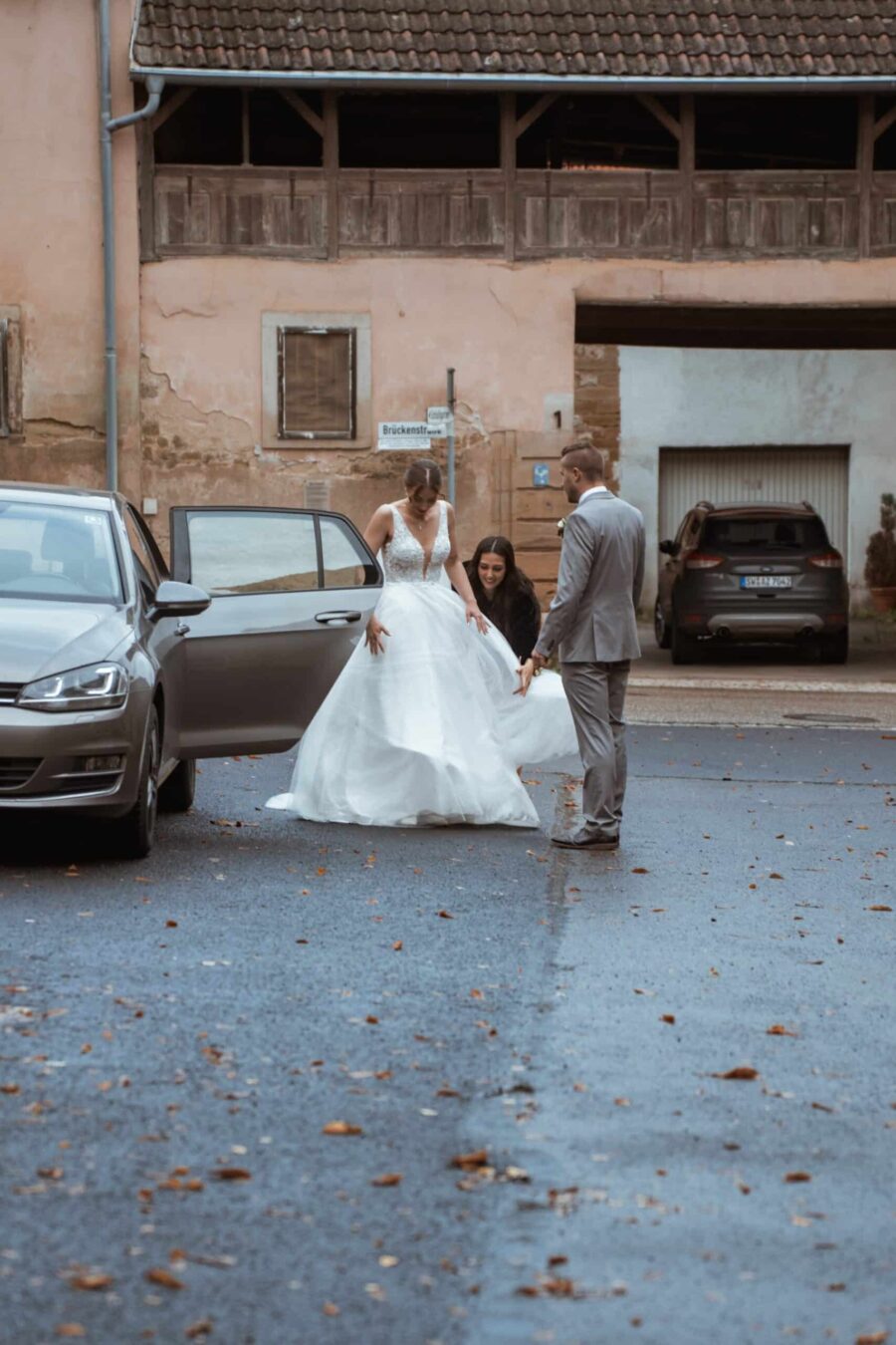 Braut im Kleid steigt aus Auto im Hof.