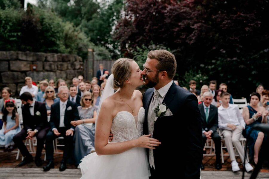 Brautpaar vor Hochzeitsgästen im Freien.