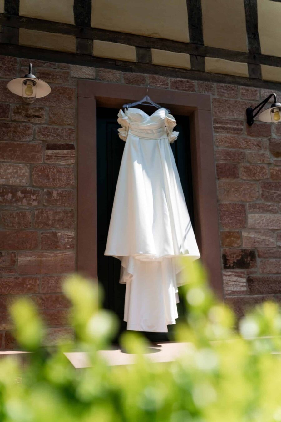 Brautkleid hängt vor rustikaler Mauer, Hofgut Hünersdorff