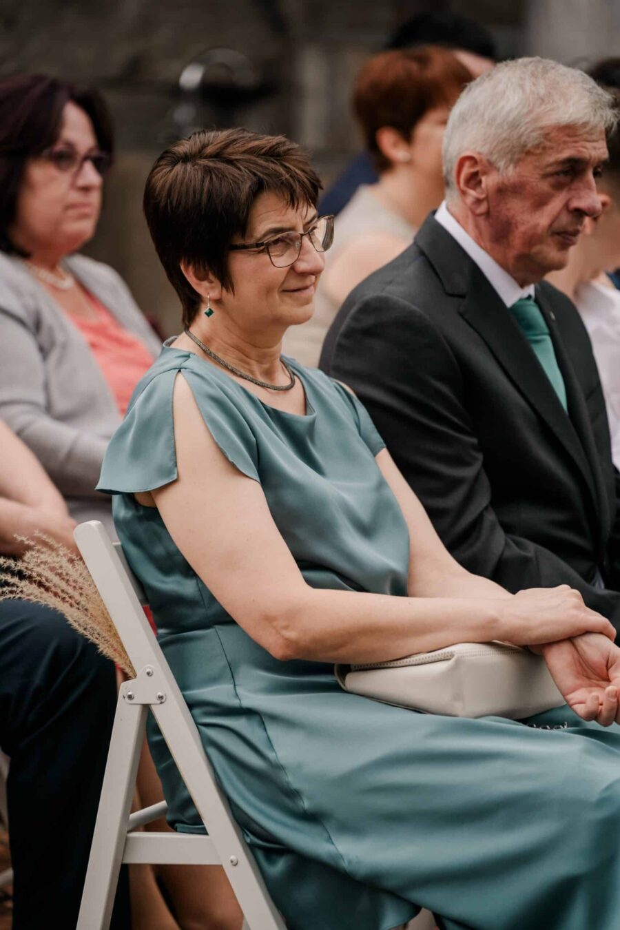 Hochzeitsgäste in festlicher Kleidung auf Stühlen