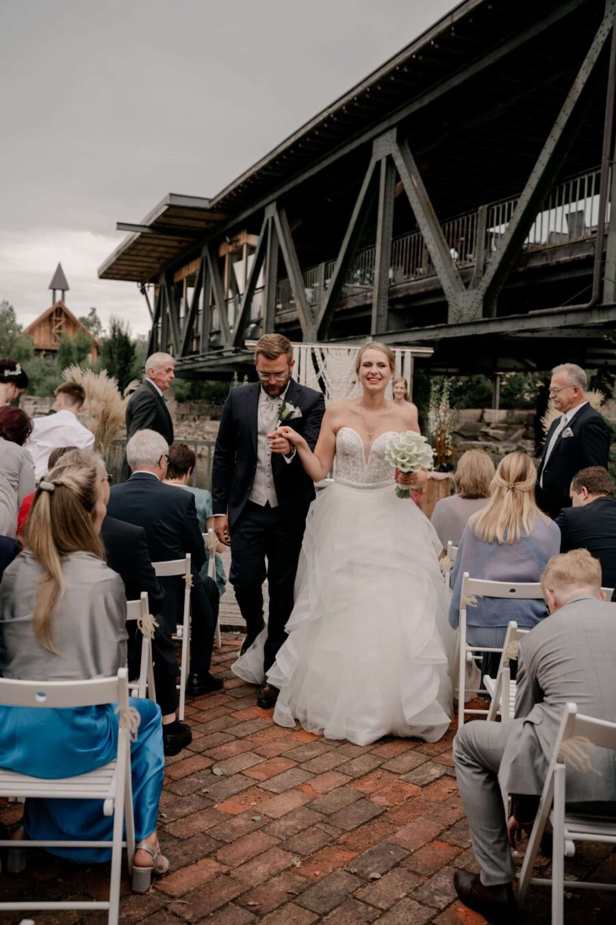 Brautpaar verlässt Zeremonie im Freien an Brücke