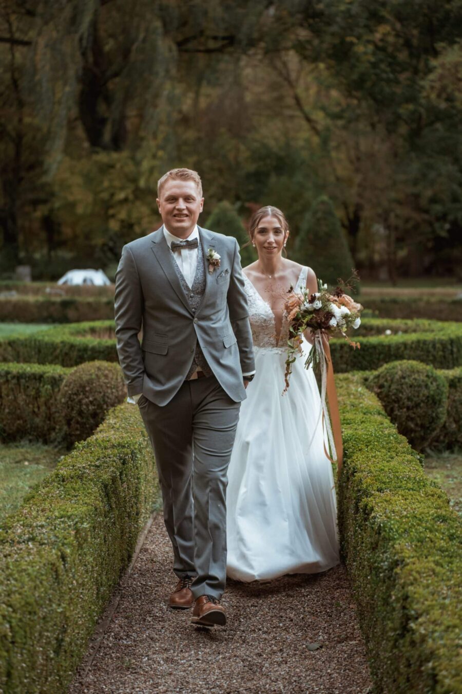 Brautpaar spaziert durch herbstlichen Garten.