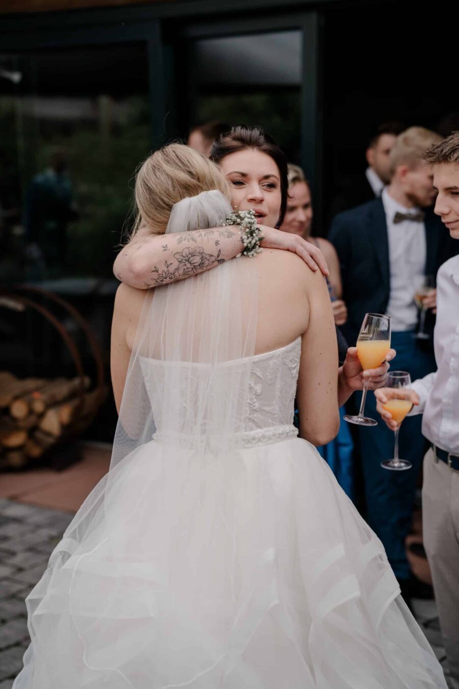 Brautpaar umarmt Gäste bei Hochzeitsfeier draußen.