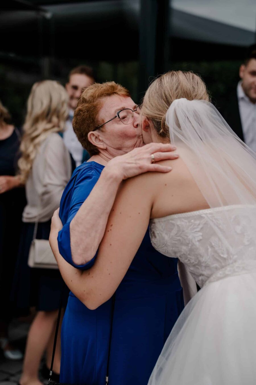 Brautpaar umarmt ältere Dame in Feierlocation