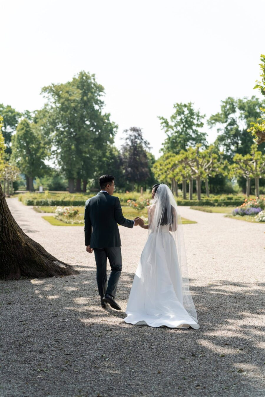 Brautpaar spaziert durch sommerlichen Garten.