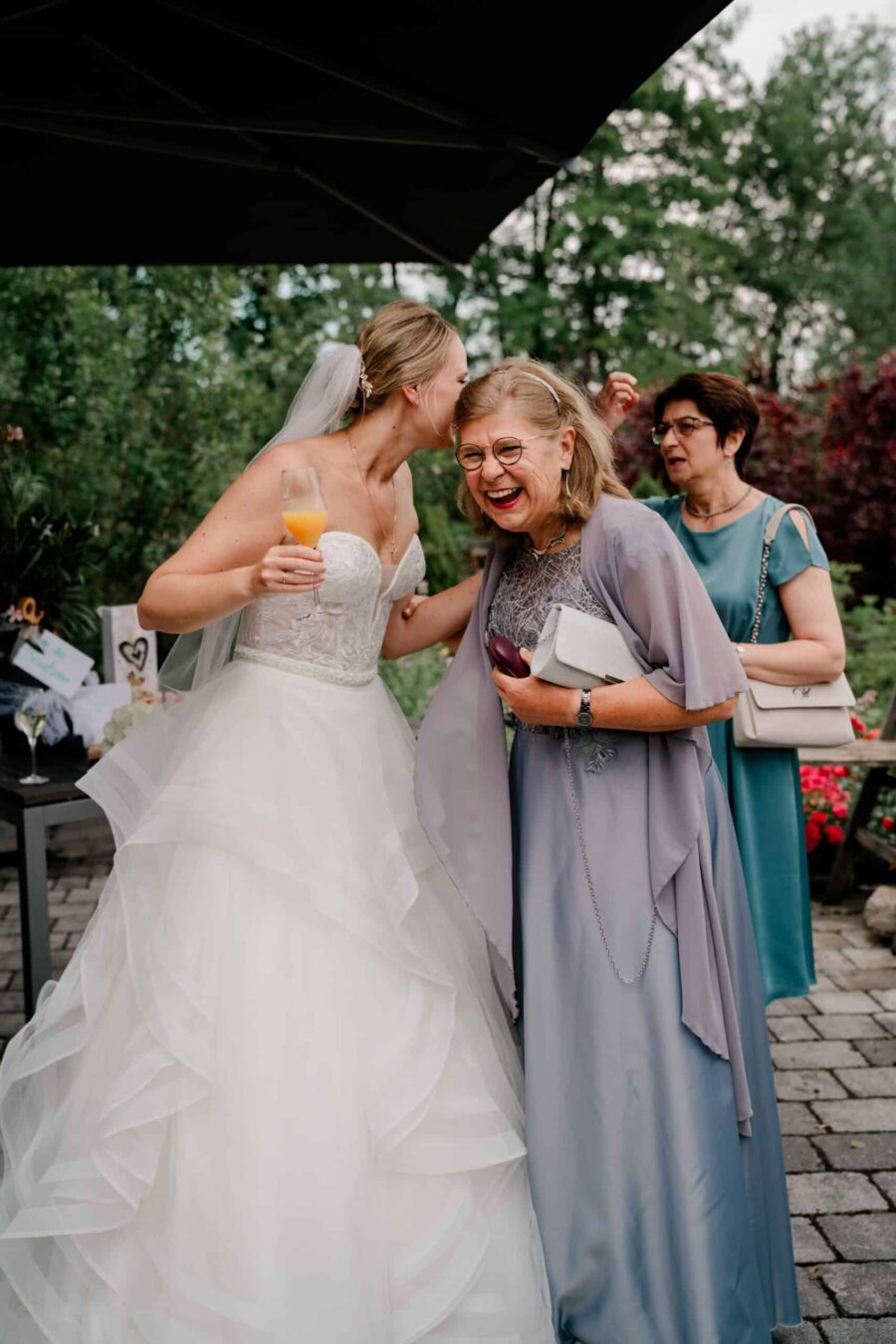 Braut lacht mit Gästen im Garten bei der Hochzeit