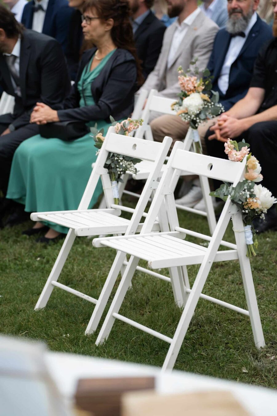 Gäste sitzen auf Hochzeitsstühlen mit Blumenschmuck