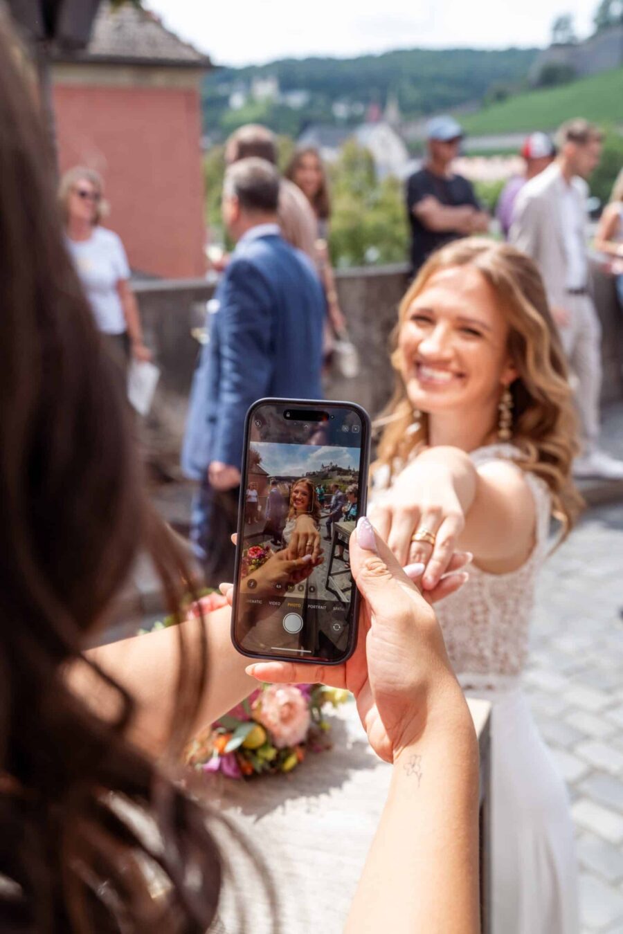 Braut zeigt Ring mit Handyfoto im Freien