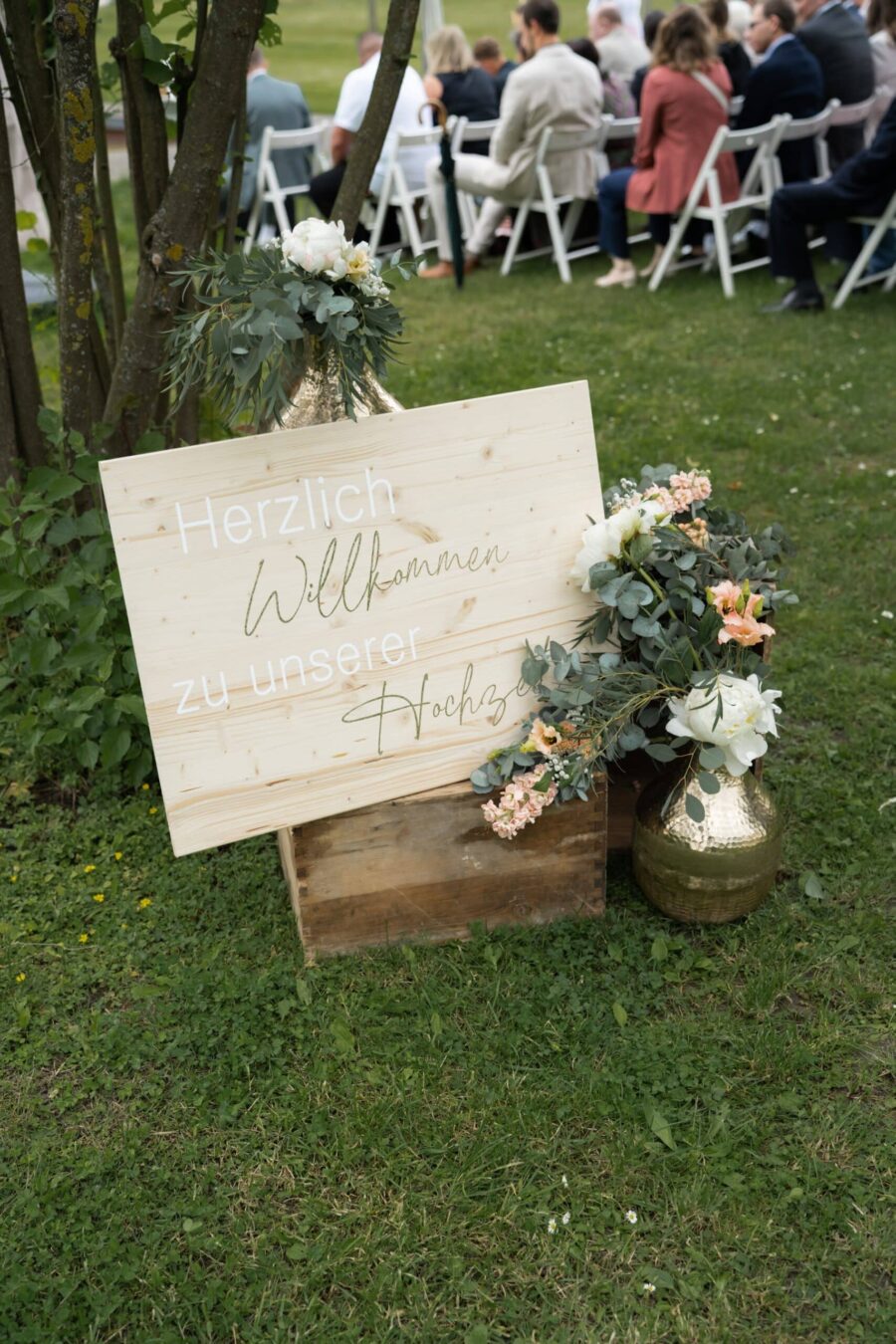 Hochzeitsschild mit Blumenarrangement im Garten