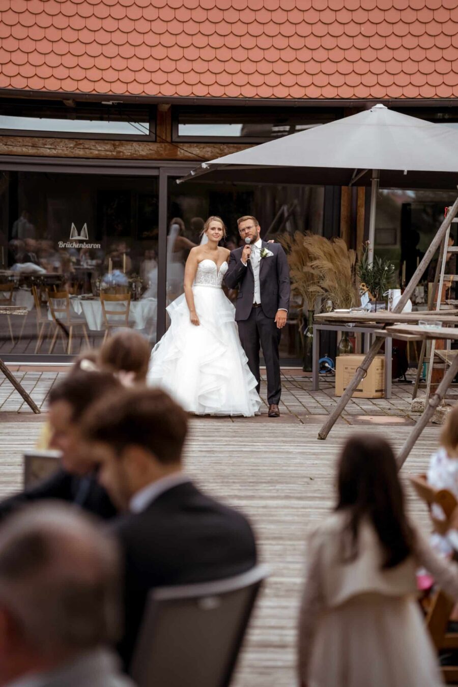 Hochzeitspaar spricht vor Gästen auf Terrasse