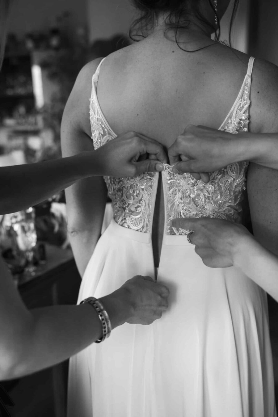 Brautkleid wird zugeknöpft von helfenden Händen.