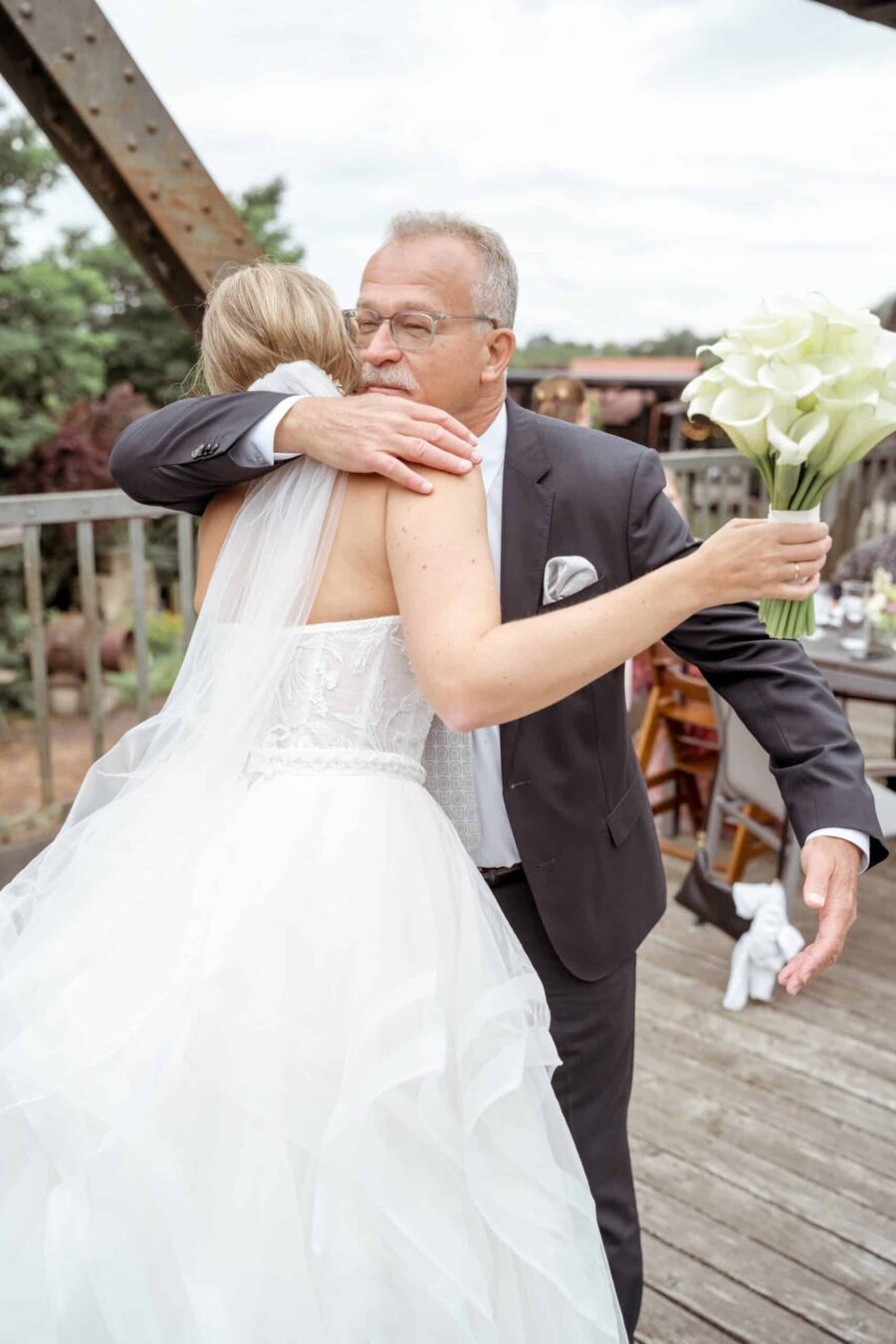 Braut umarmt Gast mit Blumenstrauß auf Terrasse