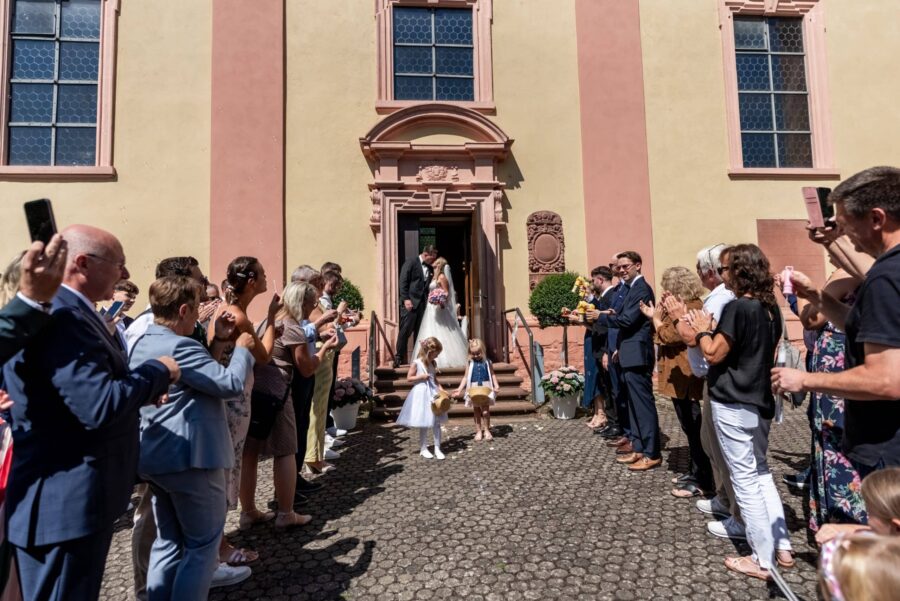 Hochzeitsgesellschaft begrüßt Brautpaar vor Kirche