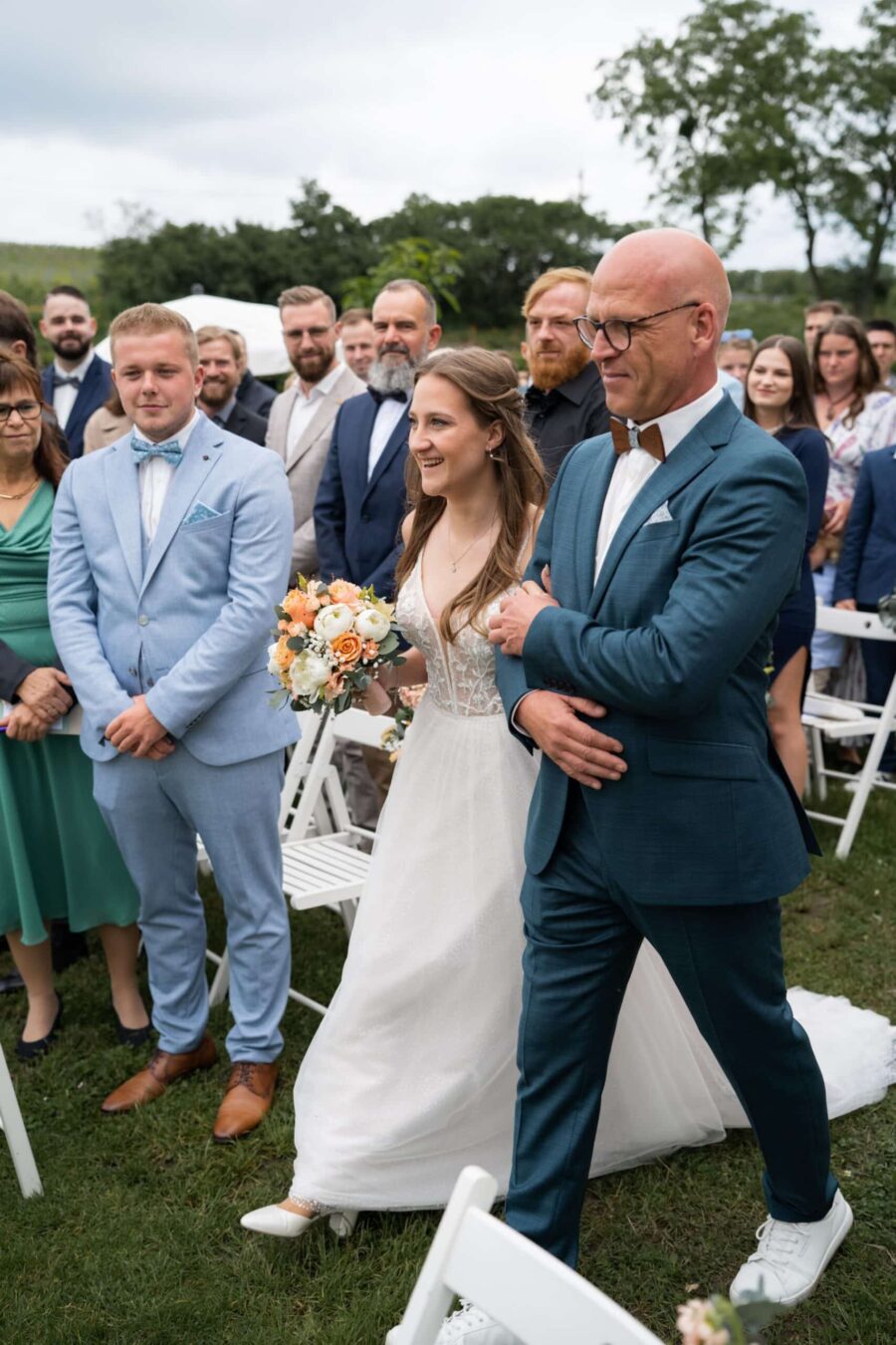 Braut mit Blumenstrauß schreitet zum Traualtar im Freien