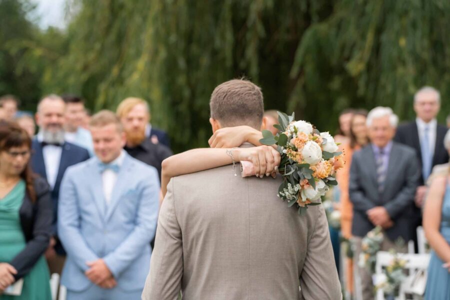 Brautpaar umarmt sich mit Blumenstrauß im Freien