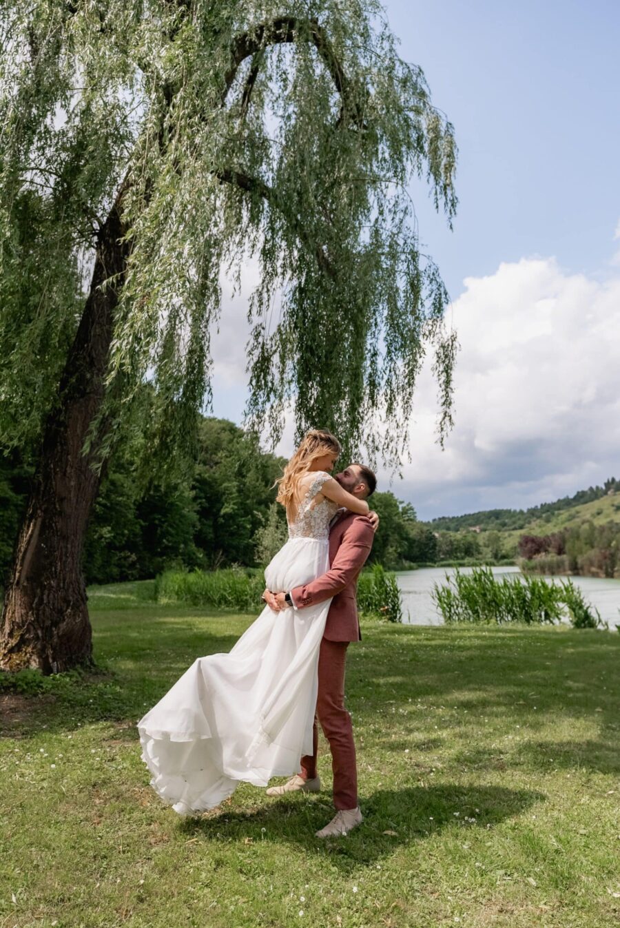 Brautpaar umarmt sich am Seeufer im Grünen