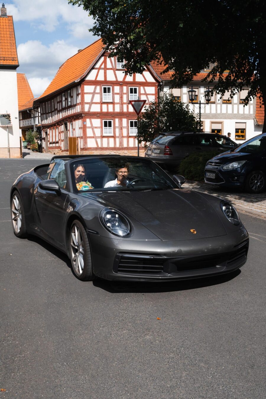 Brautpaar im Cabrio vor Fachwerkhäusern