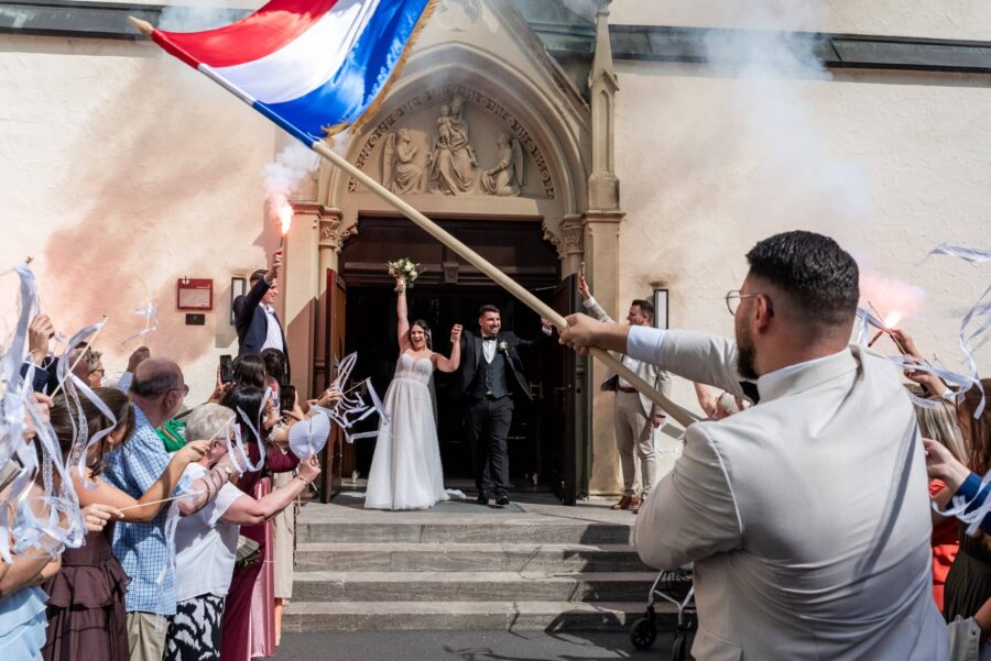 Brautpaar verlässt Kirche mit jubelnden Gästen.