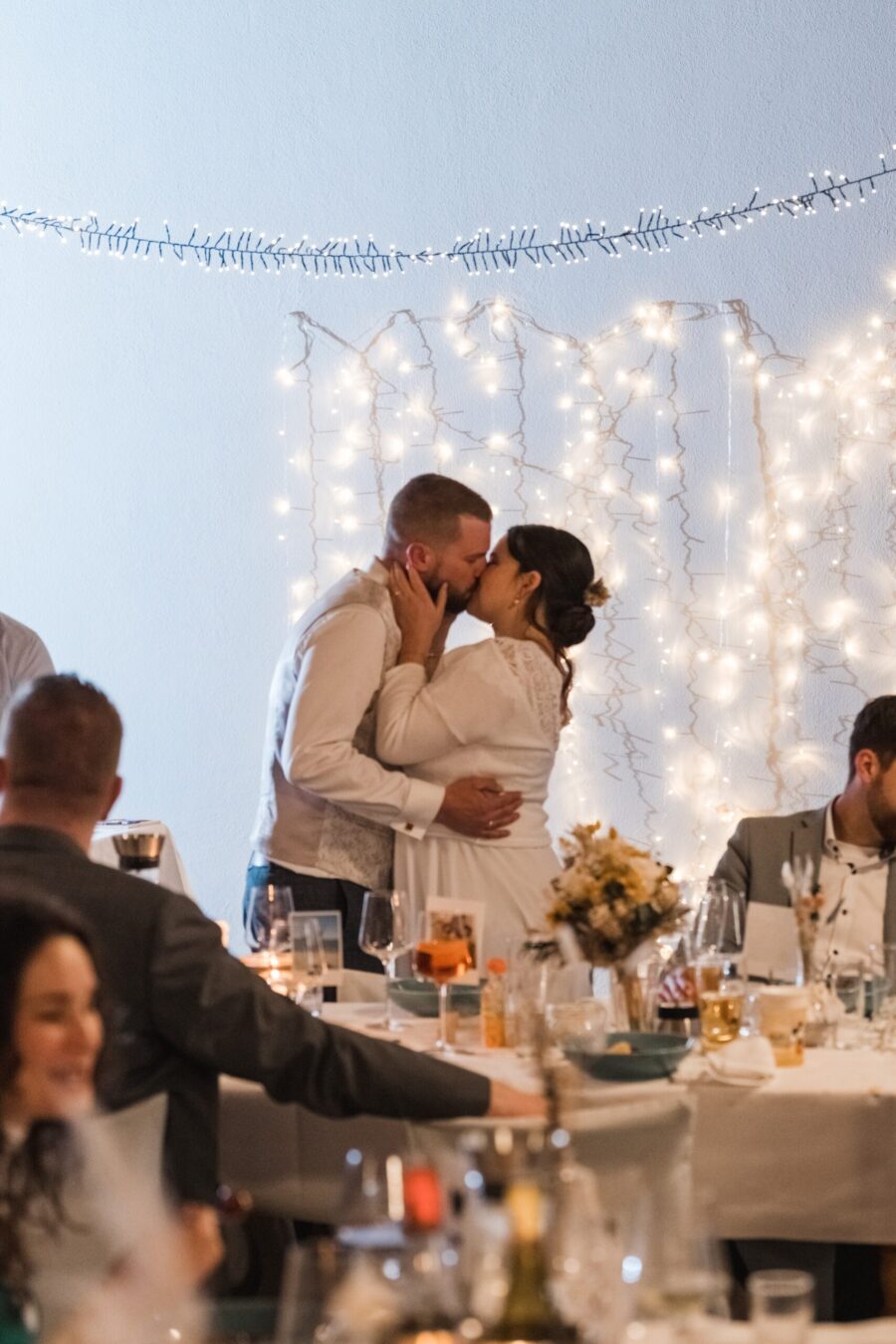 Brautpaar küsst sich vor Lichterketten im Saal