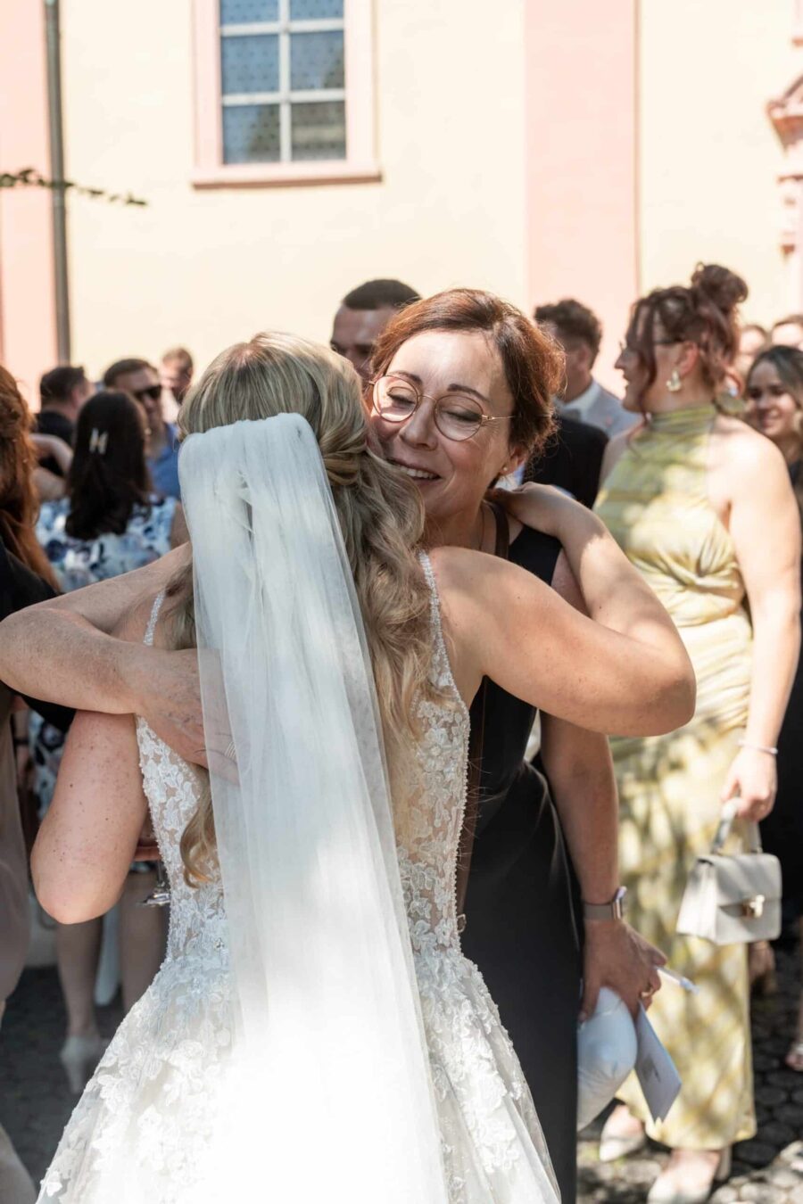 Braut umarmt Hochzeitsgast vor Kirche.