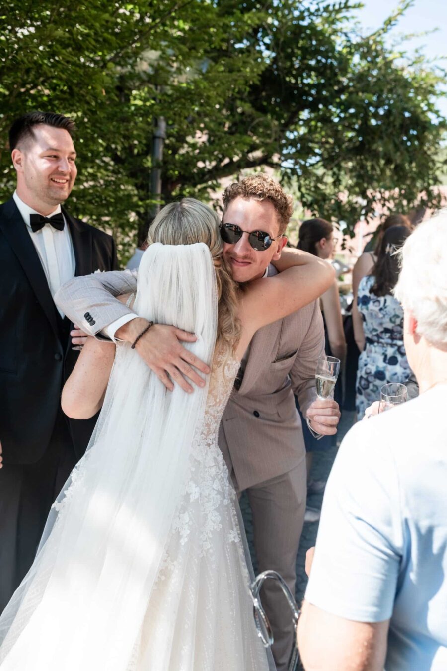 Brautpaar umarmt Gäste im sonnigen Garten