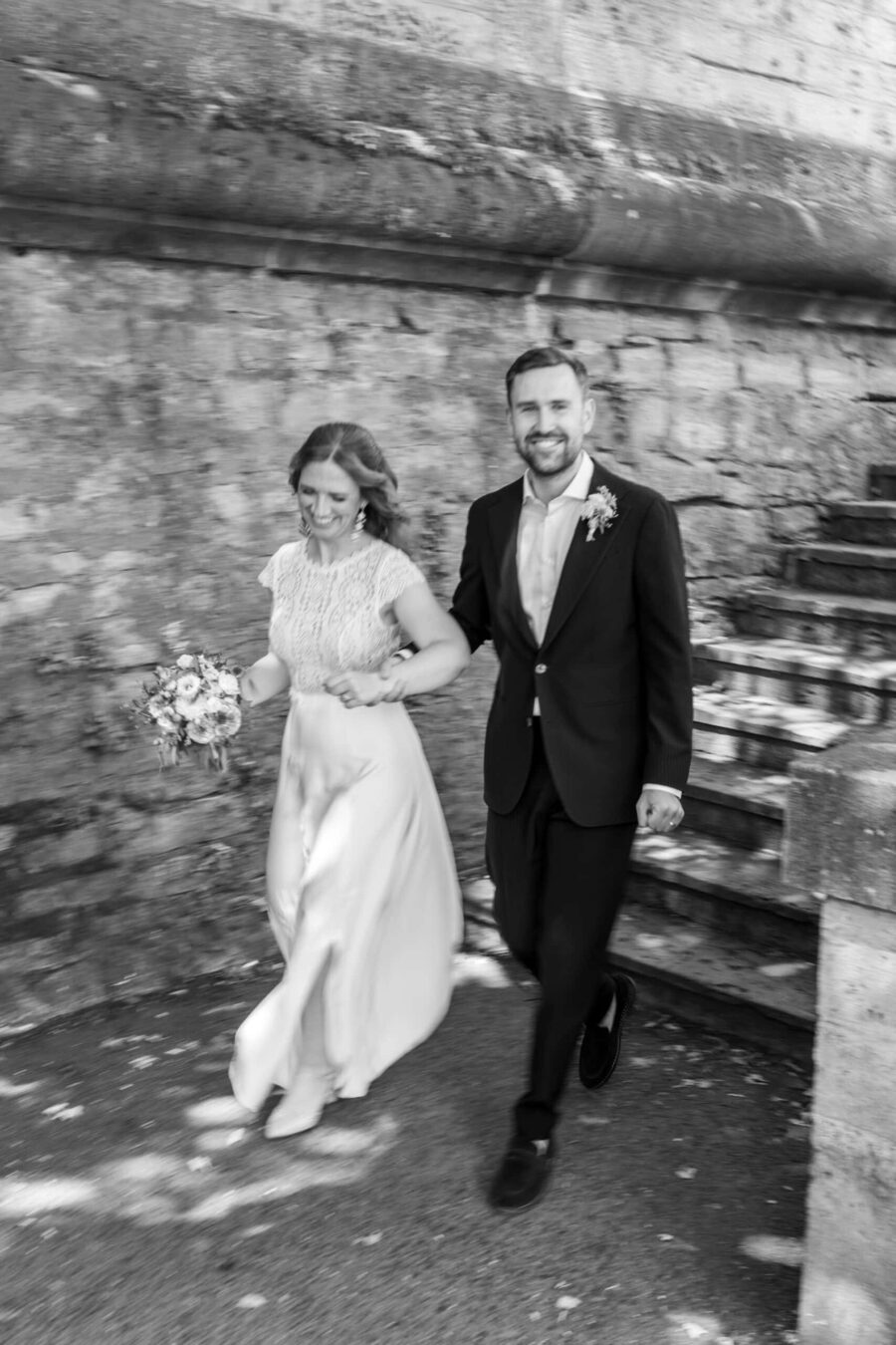 Hochzeit Steinburg Würzburg | Editorial Style & Party | Florian Knusper 110 Brautpaar läuft fröhlich an Steinmauer entlang