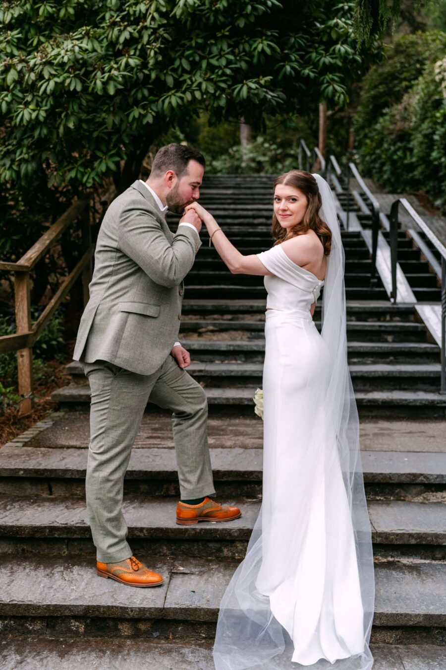 Hochzeit Insel Mainau Bodensee – Heiraten am Bodensee 26 Bräutigam küsst Hand der Braut auf Steintreppe im Garten