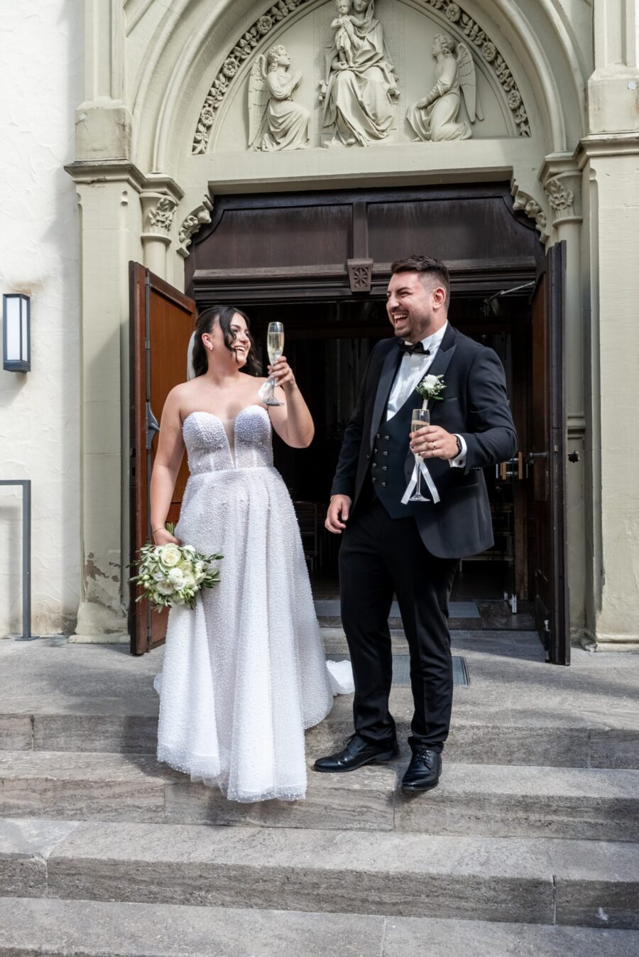 Brautpaar beim Anstoßen vor einer Kirche