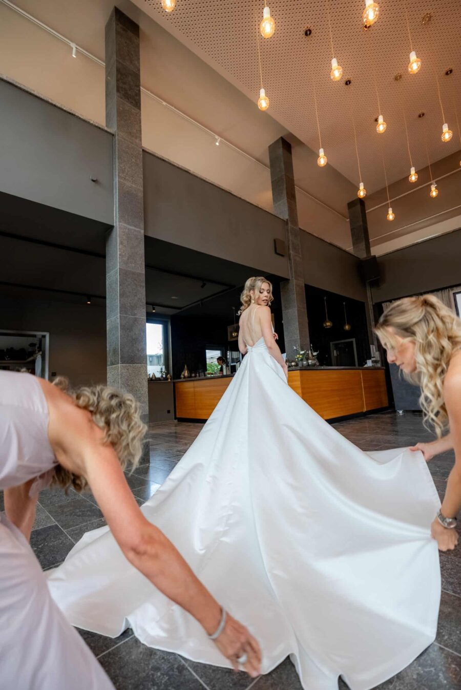 Braut im weißen Kleid mit Helferinnen in moderner Halle