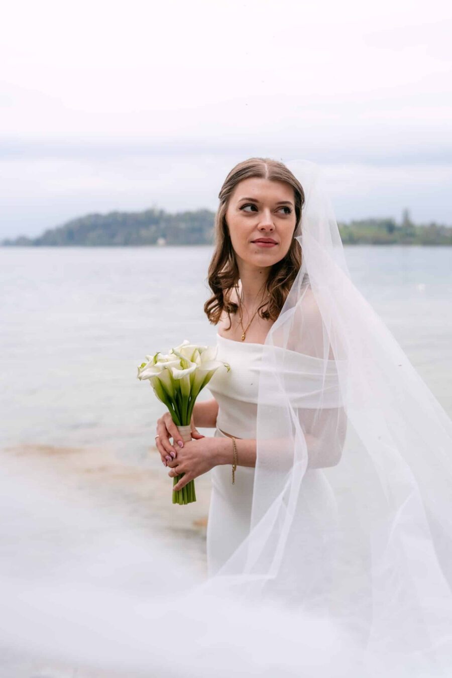 Braut mit Schleier und Calla-Lilien am Seeufer