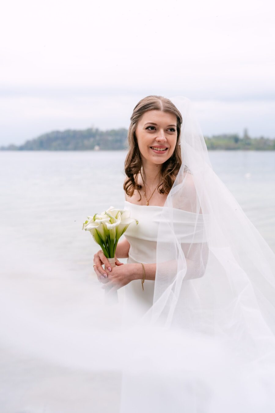 Braut mit Schleier und Calla-Strauß am Seeufer