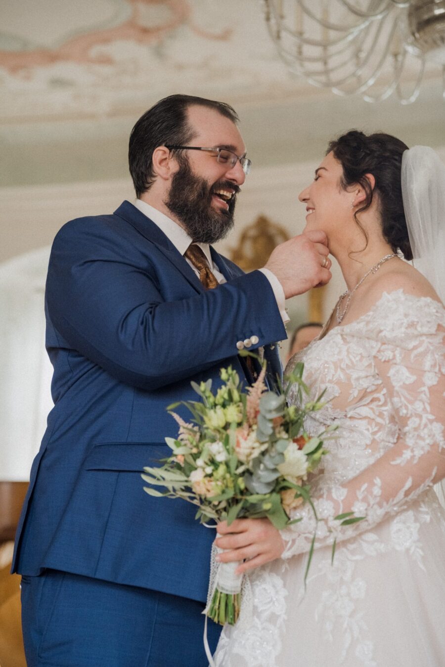 Brautpaar lächelt, hält Blumenstrauß in edlem Saal.