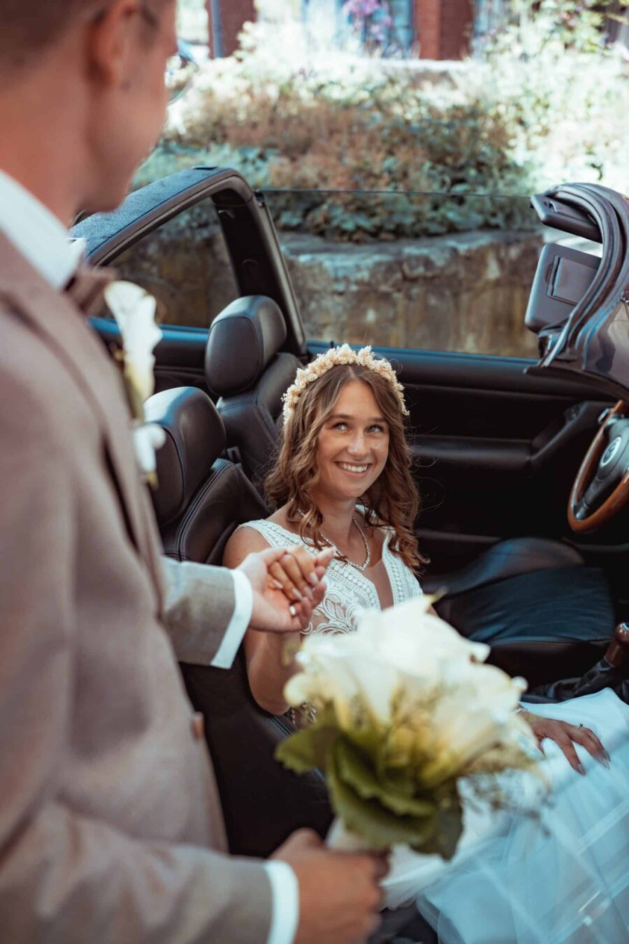 Braut im Cabrio mit Blumenstrauß und Bräutigam