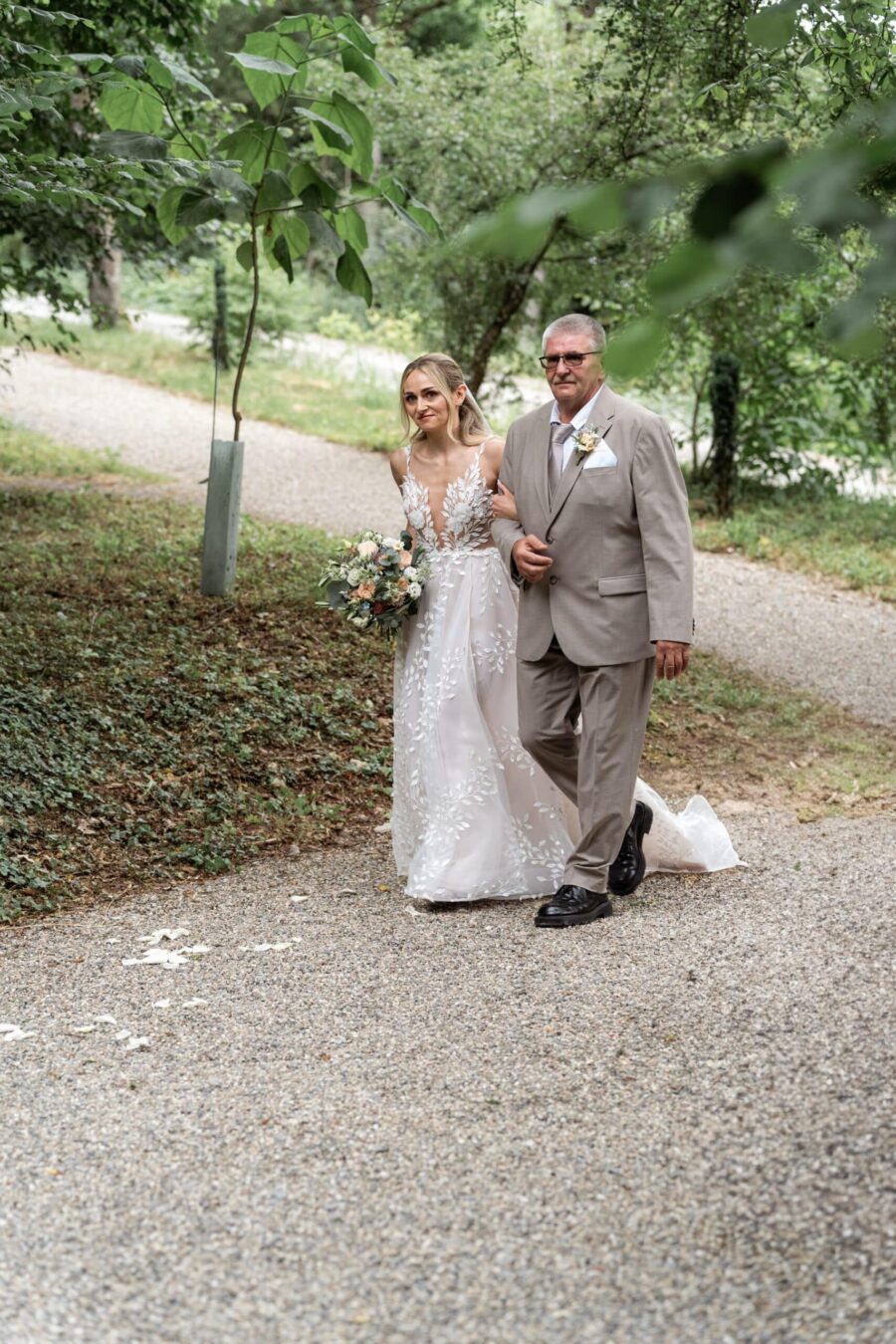 Braut mit Begleiter auf Gartenweg bei Hochzeit