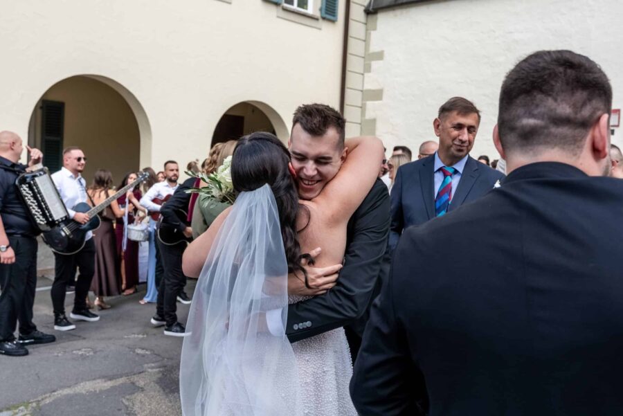 Brautpaar umarmt sich vor Hochzeitsgästen.