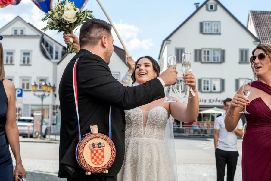 Brautpaar beim Anstoßen mit Gästen draußen