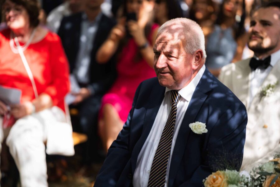 Älterer Hochzeitsgast im Anzug draußen.