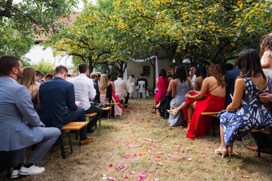 Gartenhochzeit mit Gästen auf Bänken unter Bäumen