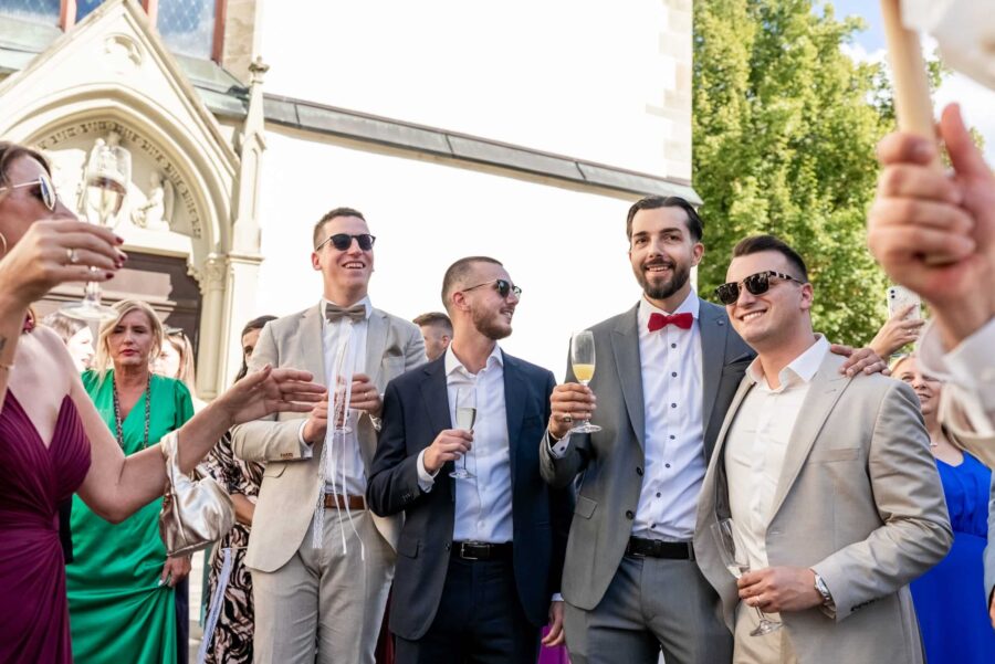 Hochzeitsgäste mit Sekt und Festtagskleidung draußen
