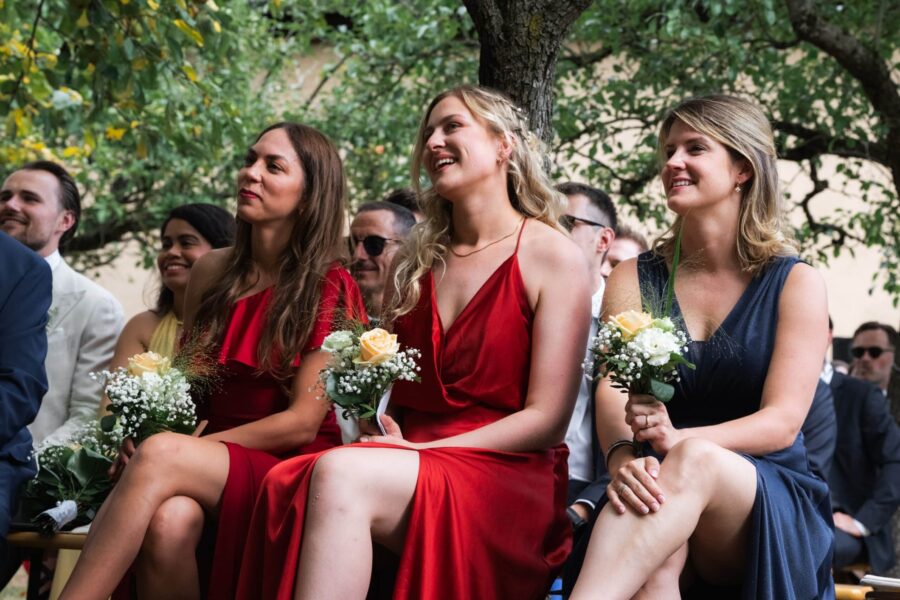 Hochzeitsgäste lachend mit Blumensträußen im Freien