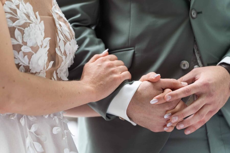 Verschränkte Hände des Brautpaars in eleganter Kleidung