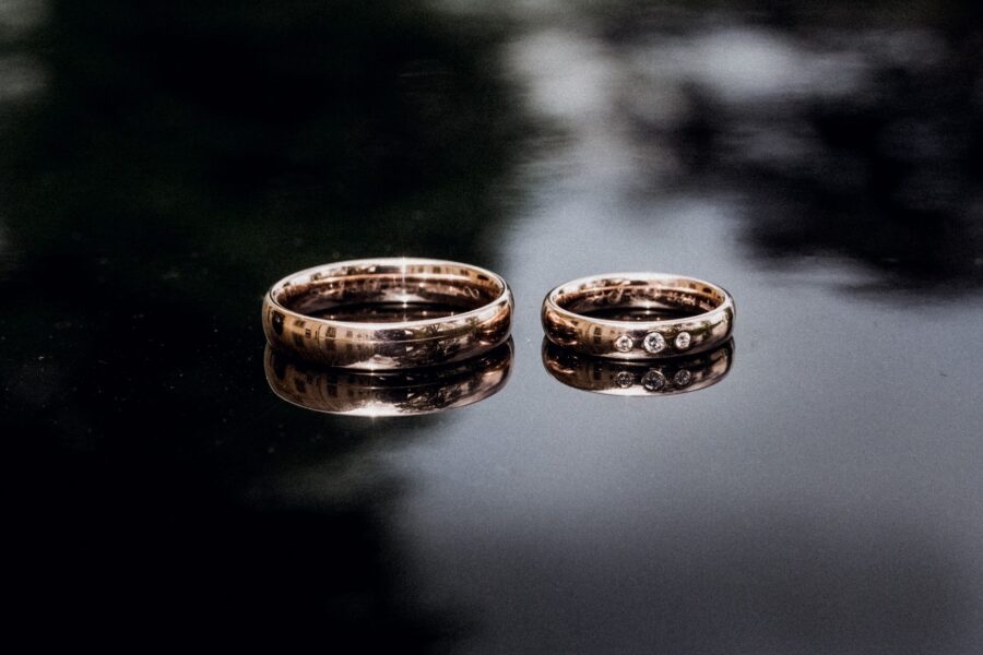 Zwei goldene Eheringe auf spiegelnder Oberfläche.