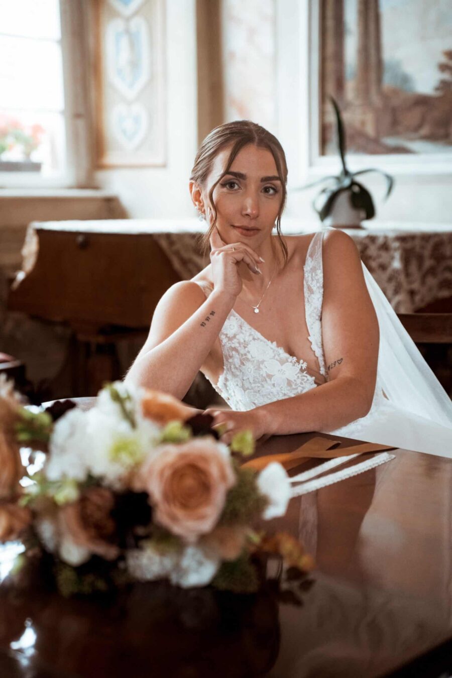 Braut in Spitzenkleid vor Blumenarrangement am Tisch