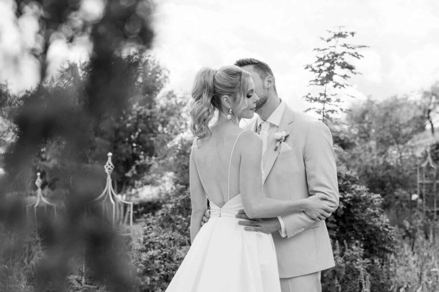 Brautpaar im Garten umarmt sich liebevoll.