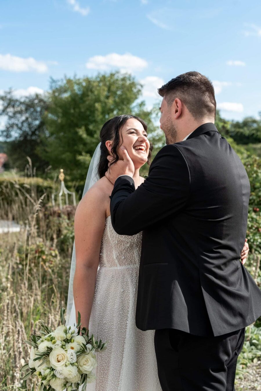 Brautpaar lächelnd im Garten mit Blumenstrauß