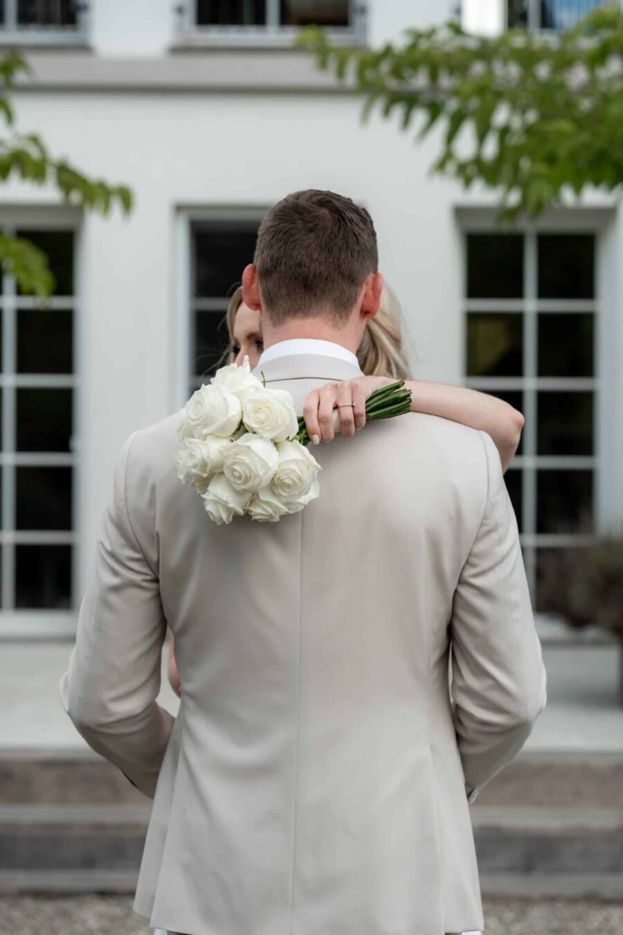 Brautpaar umarmt sich mit Rosenstrauß im Garten
