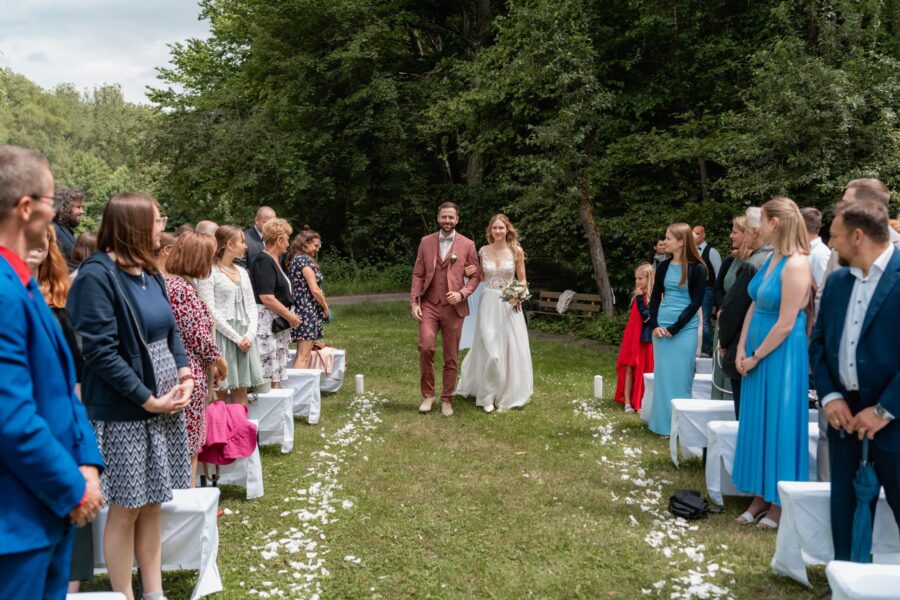 Brautpaar schreitet durch Allee im Garten mit Gästen